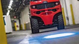 Un carrello elevatore controbilanciato Linde con BlueSpot proietta un punto di segnalazione blu sul pavimento del capannone