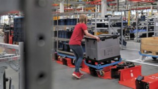 L’operatrice carica il rimorchio di un trenino di movimentazione con un carrello di mezza misura