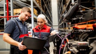 Due tecnici dell'assistenza di Linde Material Handling guardano un computer portatile accanto a un carrello elevatore.