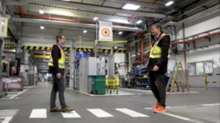 Due collaboratori si incrociano nel magazzino mentre indossano il Linde Secure Distance Vest e il Linde Distance Beeper.