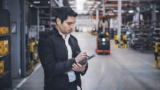 Un collaboratore di Linde Material Handling si trova nel magazzino e prende appunti sul suo tablet.