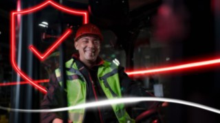 Persona con indumenti da lavoro e casco di protezione, seduta in un carrello elevatore Linde Persona con indumenti da lavoro e casco di protezione, seduta in un carrello elevatore Linde
