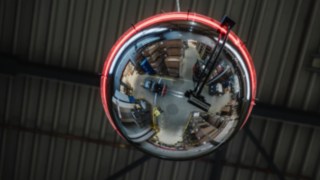 Uno specchietto rotondo con una striscia luminosa che si illumina di rosso per indicare l'avvicinarsi di un carrello elevatore. Uno specchietto rotondo con una striscia luminosa che si illumina di rosso per indicare l'avvicinarsi di un carrello elevatore.