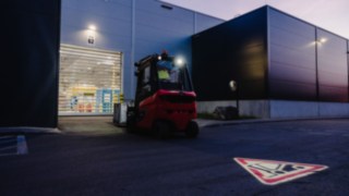 Un carrello elevatore si dirige verso il portone a serranda di un capannone all'imbrunire.