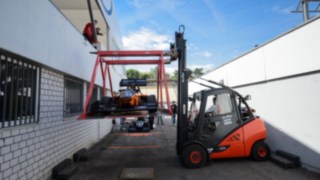 I carrelli elevatori a noleggio di Linde trasportano con cautela una macchina da corsa in un dispositivo previsto appositamente per tale scopo I carrelli elevatori a noleggio di Linde trasportano con cautela una macchina da corsa