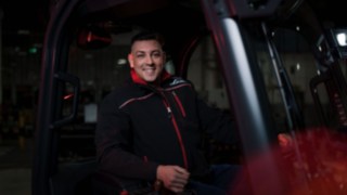 Un collaboratore di Linde Material Handling è seduto su un carrello elevatore industriale e sorride in direzione della fotocamera.