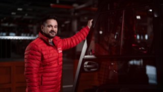 Un collaboratore di Linde Material Handling si trova accanto a un carrello elevatore industriale e sorride in direzione della fotocamera.