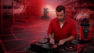Un DJ è alla console in un magazzino, con i carrelli elevatori automatizzati di Linde Material Handling sullo sfondo.