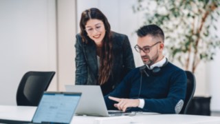 Due collaboratori si scambiano opinioni davanti a un laptop, simboleggiando un efficace lavoro di squadra con un impatto diretto sull'efficienza e la sostenibilità delle catene di fornitura globali nell'intralogistica.