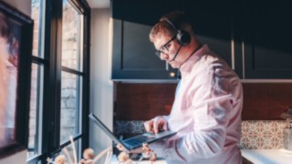 Un dipendente con cuffie lavora da casa sul proprio laptop e dimostra la flessibilità del lavoro nel settore dell'intralogistica e dell'automazione.