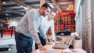 Due colleghi analizzano i piani di progetto sui loro laptop in un moderno ambiente di magazzino, dimostrando la collaborazione creativa presso KION Automation.