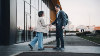 Due colleghi internazionali si salutano davanti all'edificio dell'azienda, simboleggiando il lavoro globale presso KION Automation.