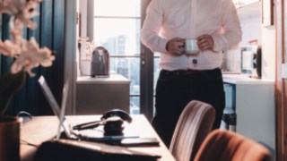 Una persona lavora da casa con una tazza di caffè in mano, rappresentando gli orari di lavoro flessibili e un sano equilibrio tra vita professionale e vita privata presso KION Automation.