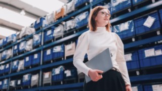 Una project manager con un laptop in un moderno magazzino si impegna a favore di catene di fornitura sostenibili ed efficienti presso KION Automation.