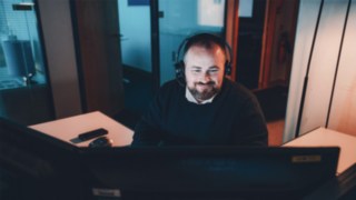 Un project manager con cuffie lavora al computer e offre uno sguardo sulla quotidianità lavorativa in Linde nel settore dell'intralogistica e dell'automazione. 