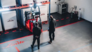 Due esperti esaminano un veicolo autonomo Linde in un magazzino dotato di attrezzature all'avanguardia, che rappresenta l'impiego di soluzioni di automazione altamente sofisticate e la partecipazione attiva all'innovazione tecnologica.