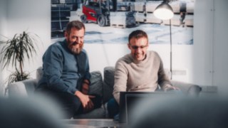 Due dipendenti sono seduti rilassati su un divano e ridono insieme guardando il contenuto di un laptop, simboleggiando un ambiente di lavoro stimolante che offre spazio alla creatività, all'innovazione e allo sviluppo personale.