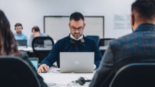 Un dipendente con cuffie lavora concentrato al computer portatile in un ufficio moderno e collaborativo, simbolo di un continuo sviluppo professionale attraverso corsi di formazione mirati e programmi di sostegno individuali.