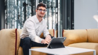 Un giovane collega lavora al tablet, seduto sul divano in un ufficio moderno. 