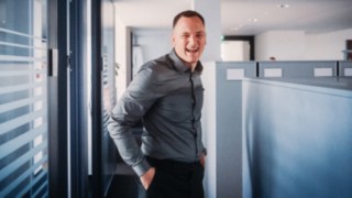 Un addetto alle vendite sorridente in un moderno ambiente d'ufficio vive la varietà e il dinamismo della quotidianità lavorativa nel settore commerciale, con contatti con clienti sempre nuovi, sfide e approcci risolutivi. 