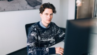 Un giovane dipendente di KION Automation è seduto concentrato davanti a un monitor in una moderna postazione di lavoro in ufficio. 