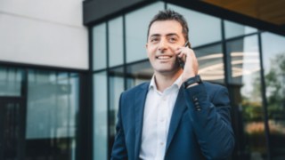 Un dipendente addetto alla messa in funzione in abito da lavoro telefona davanti a un moderno edificio adibito a uffici. 